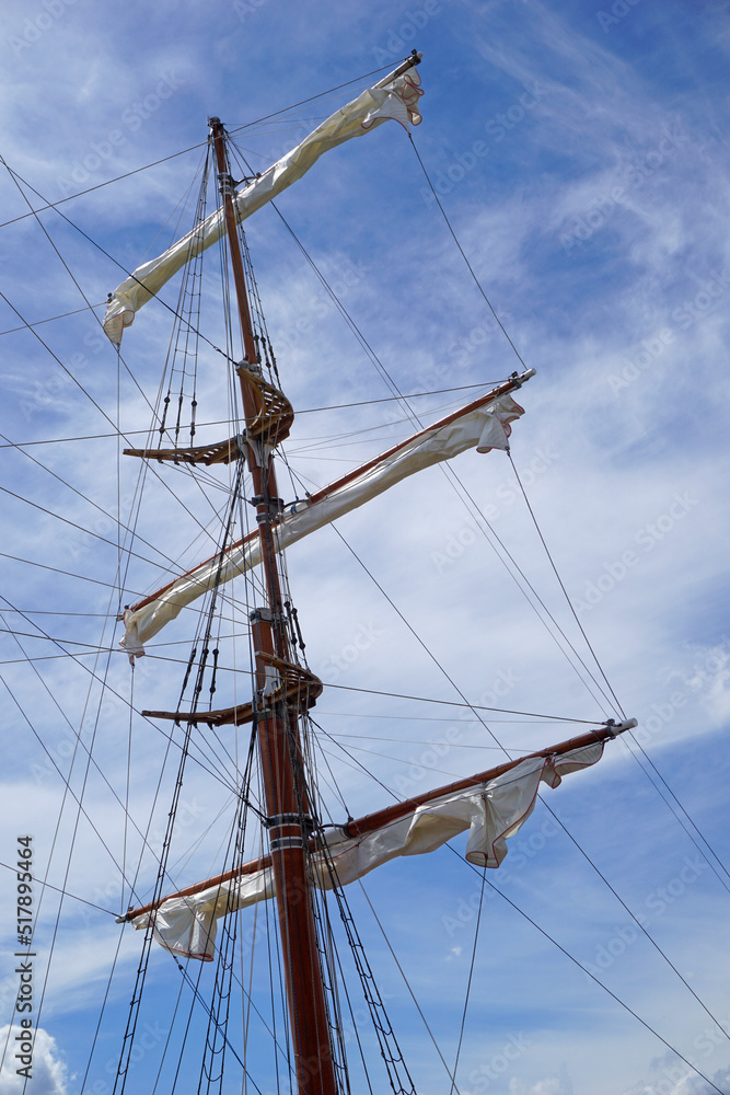 Tall ship mast with rolled sails, sky in background Tall ship mast with rolled sails, sky in background