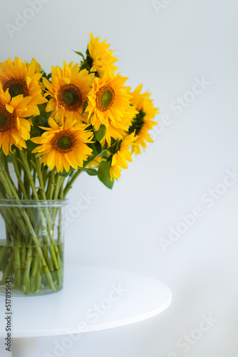 Close-up, a beautiful bouquet of traditional Ukrainian sunflower flowers in a glass vase on a white table.