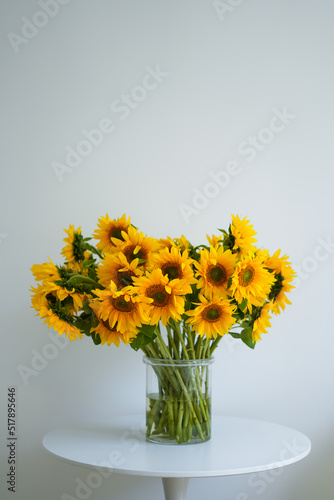 A large beautiful bouquet of traditional Ukrainian sunflower flowers in a glass vase on a white table.