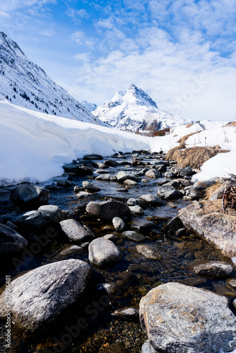 a river with stones and a lots of snow on the sides in winter, in the background a huge mountain from Galtür