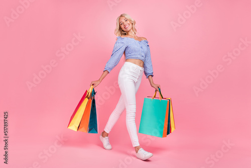 Full length photo of shiny dreamy girl dressed blue top walking holding bargains isolated pink color background