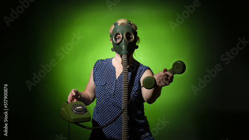 A woman in a gas mask passes the receiver of a retro phone on a dark dramatic background, hard light. © Sergey