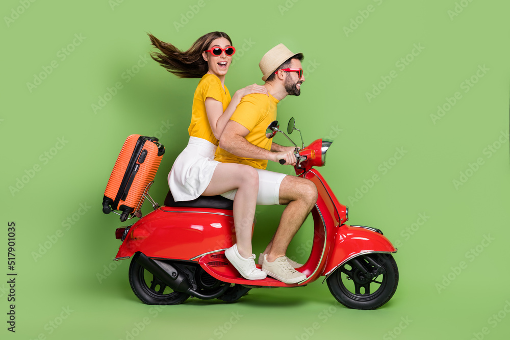 Full length profile portrait of two excited partners drive moped adventure isolated on green color background Full length profile portrait of two excited partners drive moped adventure isolated on green color background