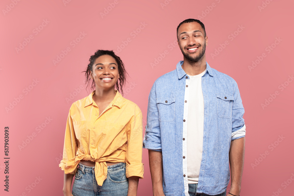 Happy mysterious african american couple looking at each other and smiling, standing isolated over pink wall Happy mysterious african american couple looking at each other and smiling, standing isolated over pink wall