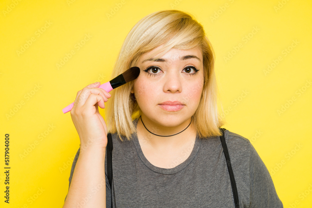 Obraz premium Closeup of a fat woman with dyed hair putting on some makeup with a brush and making eye contact