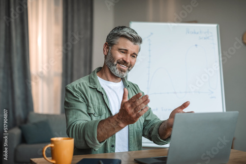 Glad old european male with beard has meeting with students or client at laptop, shoot lecture photo