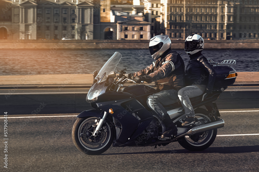 A man and a woman ride together on a sports motorcycle along the embankment. Motorcyclists travel around the city during the day on a dark blue sports bike.