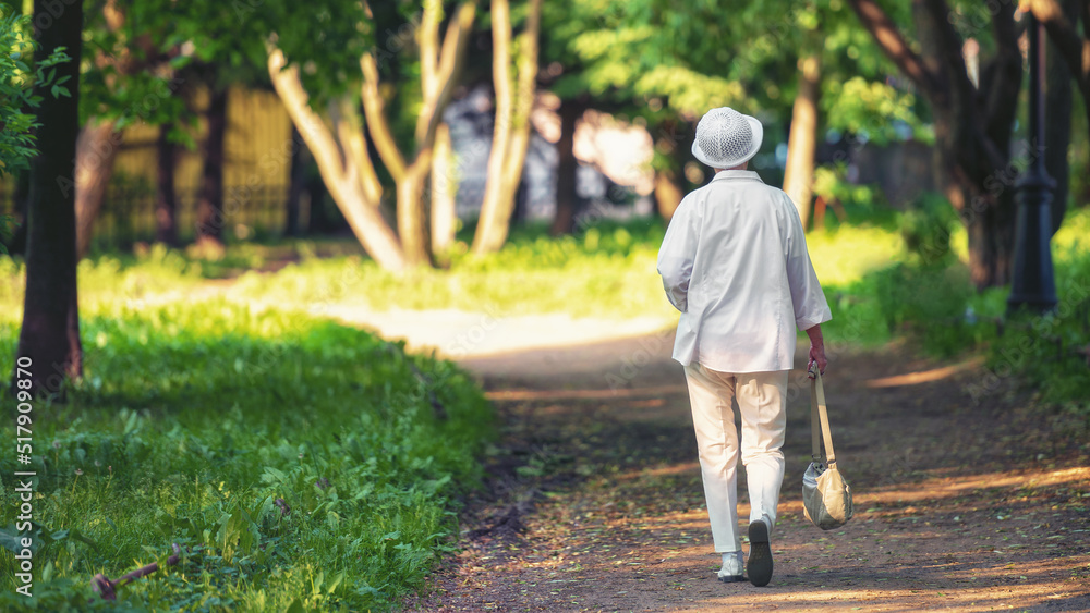 An elderly woman in white walks through a summer park. An elderly woman in white walks through a summer park.