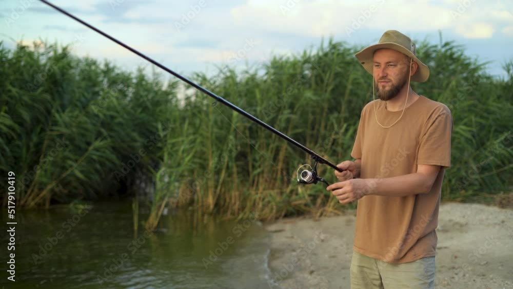 a man fisherman at sunset in a hat on the lake catches fish with a fishing rod against the background of reeds. stands and waits for a bite. Fishing holiday concept. a man fisherman at sunset in a hat on the lake catches fish with a fishing rod against the background of reeds. stands and waits for a bite. Fishing holiday concept.