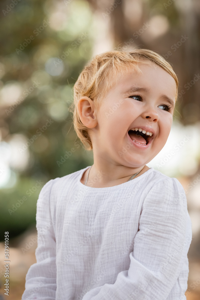 Excited toddler girl in white dress looking away outdoors. Excited toddler girl in white dress looking away outdoors.