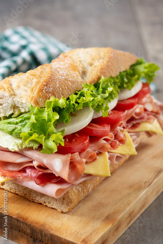 Submarine sandwich with ham, cheese, lettuce, tomatoes,onion, mortadella and sausage on wooden table	