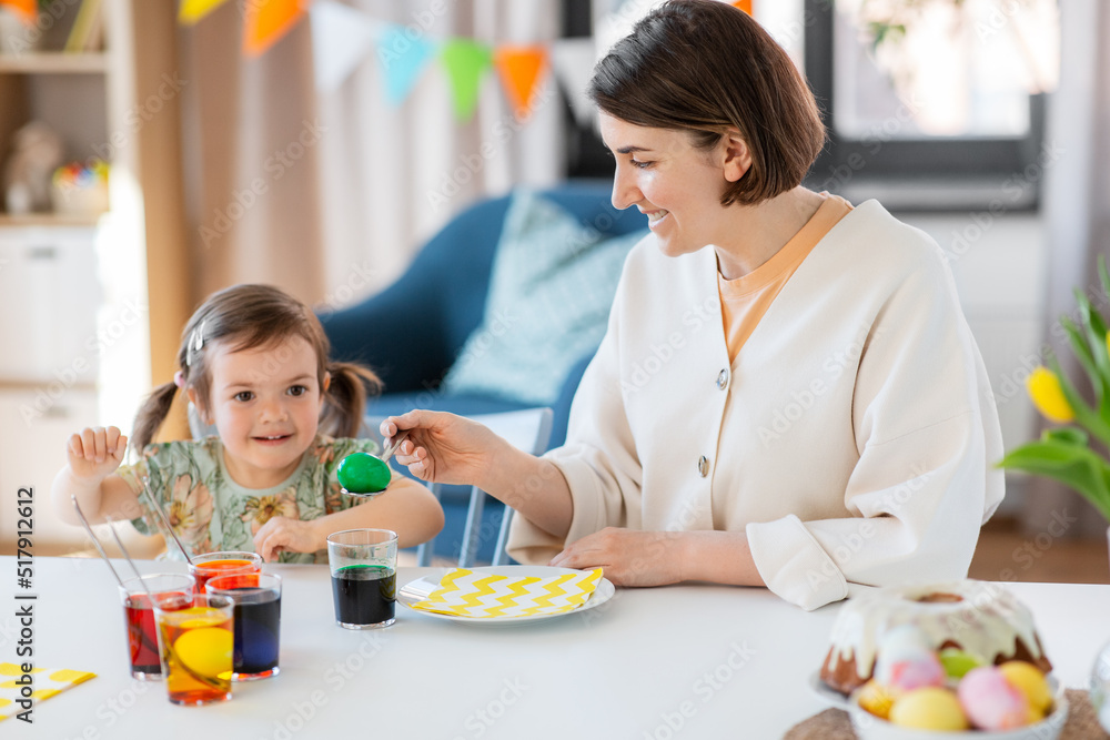 holidays, family and people concept - happy mother and little baby daughter dyeing easter eggs with colors at home holidays, family and people concept - happy mother and little baby daughter dyeing easter eggs with colors at home