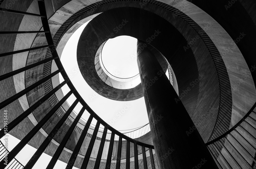 Obraz premium Bottom view of a geometric abstraction in the form of a spirally twisted metal staircase with a railing. Black and white photo