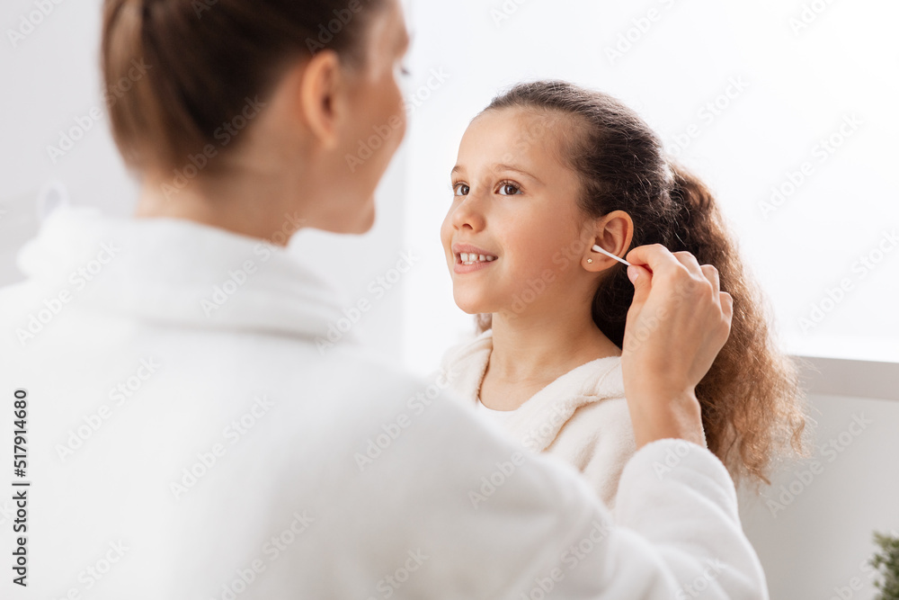beauty, hygiene, morning and people concept - happy smiling mother cleaning daughter's ear with cotton swab in bathroom beauty, hygiene, morning and people concept - happy smiling mother cleaning daughter's ear with cotton swab in bathroom