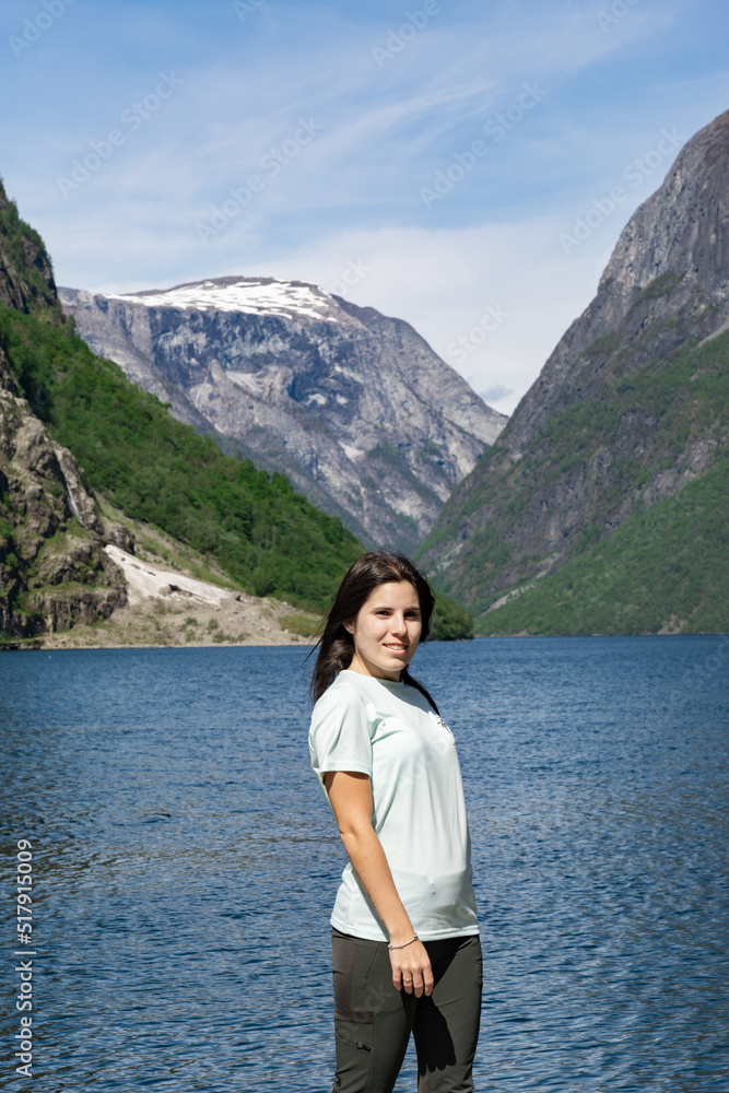Young tourist girl in the foreground and behind her the fjord with the high mountains in Gudvangen - Norway