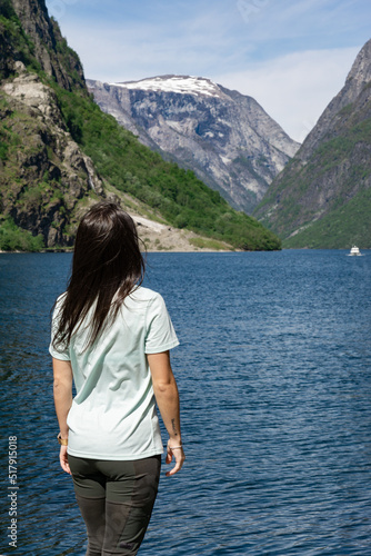 Unrecognizable young tourist girl on her back at the foot of the fjord with her arms up surrounded by high mountains in Gudvangen - Norway