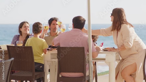 4K SlowMo - family and friends gathered for lunch enjoying a delicious paella in a bar on the beach - happy little kids playing around the table after eating, eating dessert and ice cream