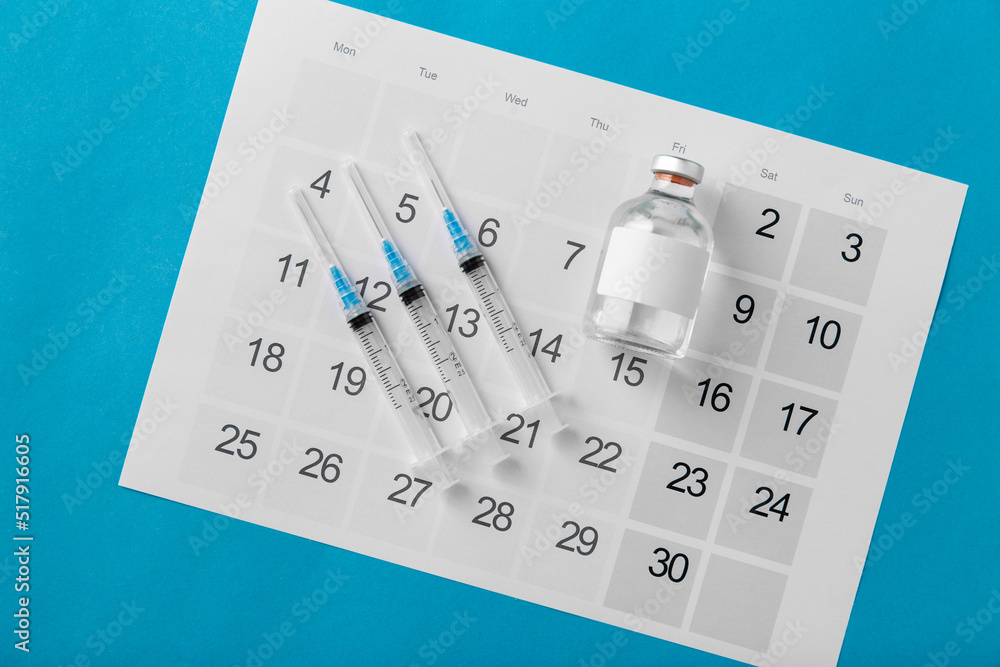 medicine, vaccination and healthcare concept - disposable syringe and calendar on blue background medicine, vaccination and healthcare concept - disposable syringe and calendar on blue background