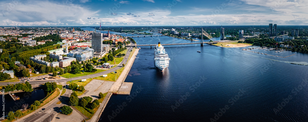 Riga, Latvia. July 18, 2022. Aerial drone view of the large cruise ship in Riga port, Latvia view to the old town and city center. - obrazy, fototapety, plakaty 