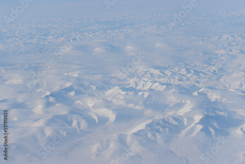 Aerial view of snow-capped mountains and clouds. Winter snowy mountain landscape. Travel to the far north of Russia. Kolyma Mountains, Magadan Region, Siberia, Russian Far East. Beautiful background.