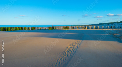 Fototapeta Naklejka Na Ścianę i Meble -  Sand  beach along a sea under a blue sky at a bright sunrise in summer, Walcheren, Zeeland, the Netherlands, July, 2022