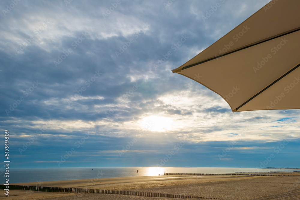 Sand  beach and sand dunes along a sea under a dusk cloudy sky at a bright sunset in summer, Walcheren, Zeeland, the Netherlands, July, 2022