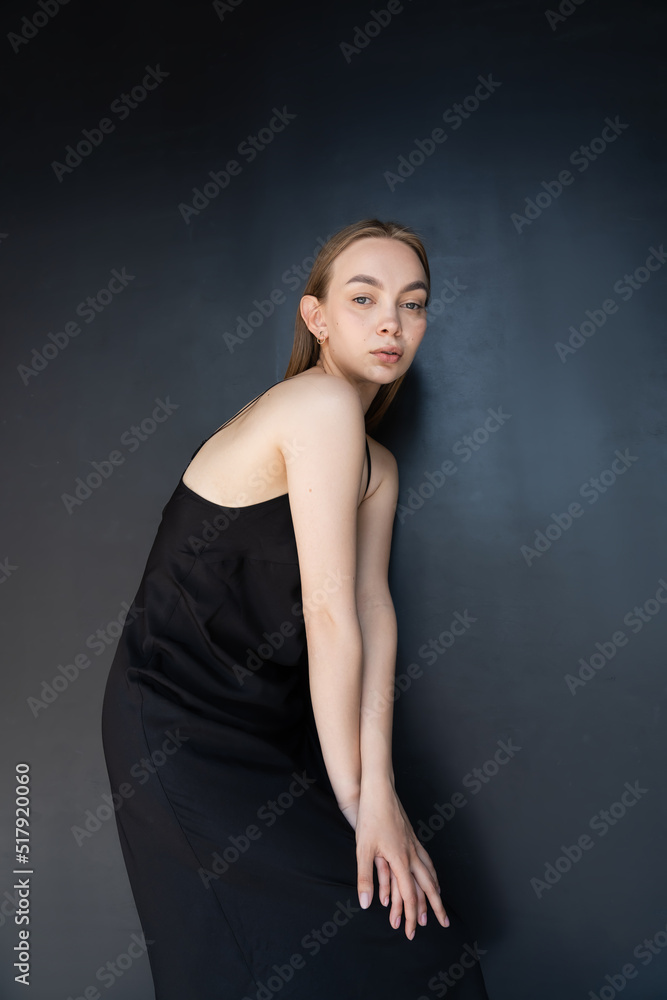 trendy woman in strap dress looking at camera while posing on black background. trendy woman in strap dress looking at camera while posing on black background.
