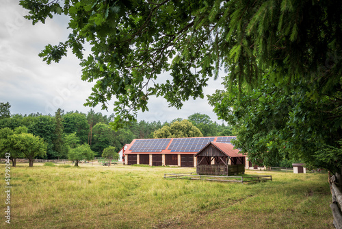 A huge brick barn with solar panels on the roof. Horse stud in Florianka. Beautiful rural landscape. The horse run in the foreground