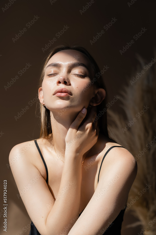 Fototapeta premium seductive woman with closed eyes and natural makeup touching neck on dark background.