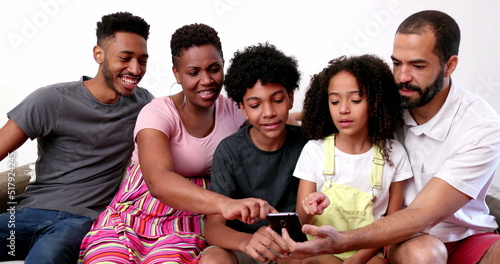 Happy African interracial family holding smartphone. Parents and kids looking at cellphone at home sofa