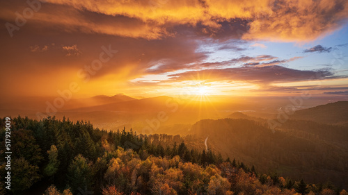 The sun shines through a gap in the cloudy sky and colours a departing thunderstorm in golden shades