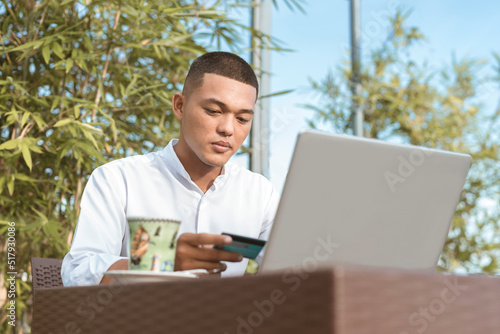 A young professional yuppie uses his debit card to make an online purchase or booking a hotel or flight. During his down time during remote field work photo