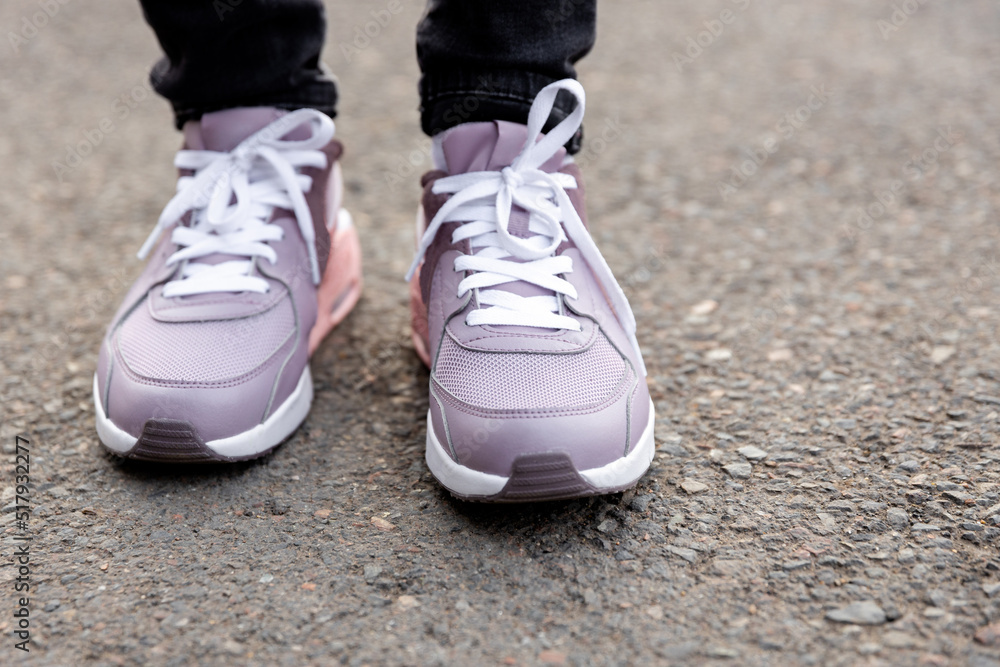 cropped image of female legs in shoes. Woman in black jeans and pink sneakers stands on pavement