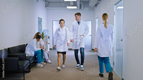 Female and man doctors walking through the modern corridor in the hospital some other nurses and doctor on the chair have a discussing as well