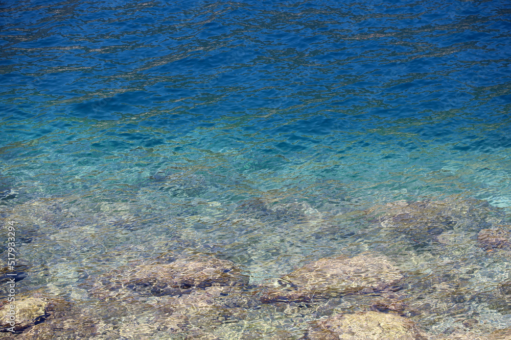 Transparent sea surface with stones on a bottom. Rocky beach, turquoise water for background Transparent sea surface with stones on a bottom. Rocky beach, turquoise water for background