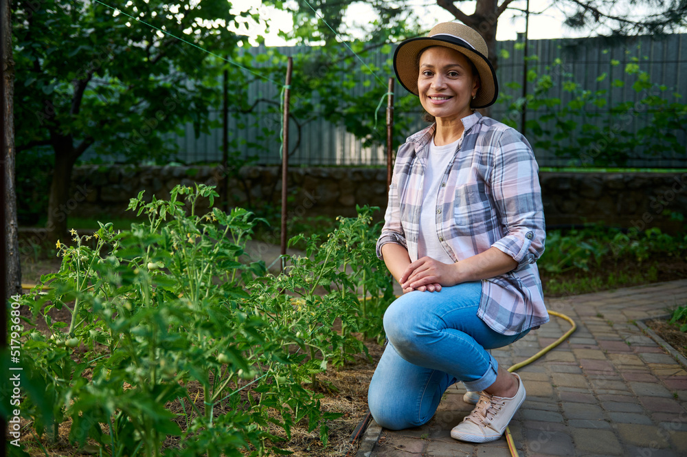 Attractive successful woman, ecological farm owner , sits next to tomato seedlings and smiles sweetly, looking at camera Attractive successful woman, ecological farm owner , sits next to tomato seedlings and smiles sweetly, looking at camera