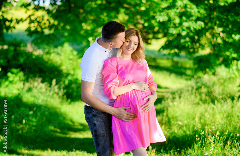 Naklejka premium Beautiful young couple of a man and a pregnant woman in the forest at sunset