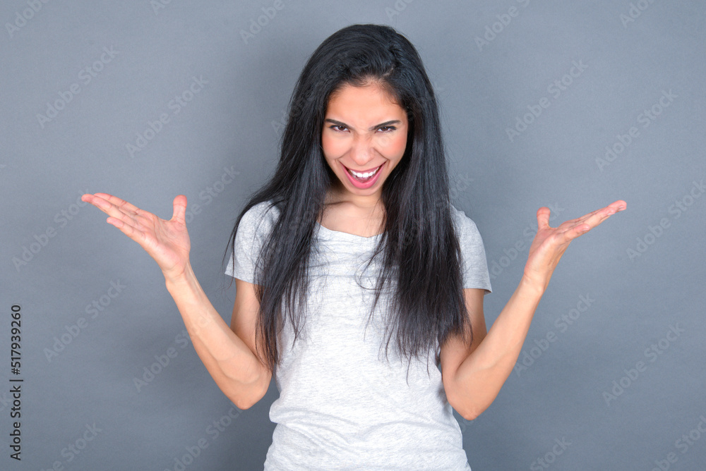 Crazy outraged young beautiful brunette woman wearing white t-shirt over grey background screams loudly and gestures angrily yells furiously. Negative human emotions feelings concept Crazy outraged young beautiful brunette woman wearing white t-shirt over grey background screams loudly and gestures angrily yells furiously. Negative human emotions feelings concept