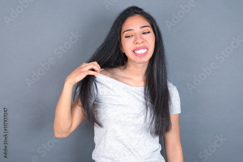 young beautiful brunette woman wearing white t-shirt over grey background stressed, anxious, tired and frustrated, pulling shirt neck, looking frustrated with problem