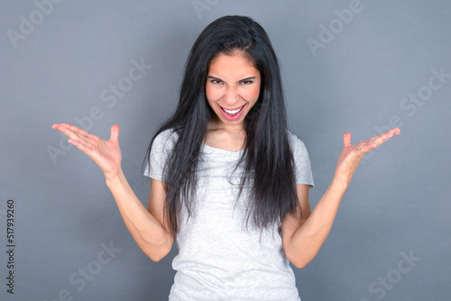Crazy outraged young beautiful brunette woman wearing white t-shirt over grey background screams loudly and gestures angrily yells furiously. Negative human emotions feelings concept