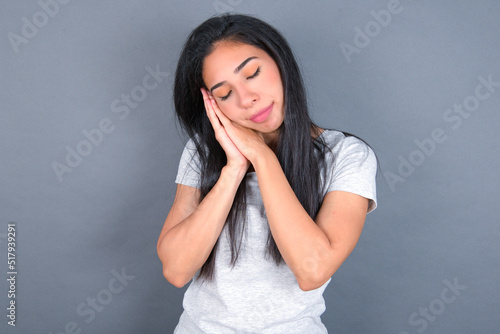 young beautiful brunette woman wearing white t-shirt over grey background leans on pressed palms closes eyes and has pleasant smile dreams about something © Jihan