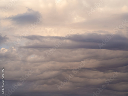 Gray cumulus clouds are a continuous wave cover of the sky. Beautiful sky with gloomy clouds in summer early in the morning. Abstract natural cloud background