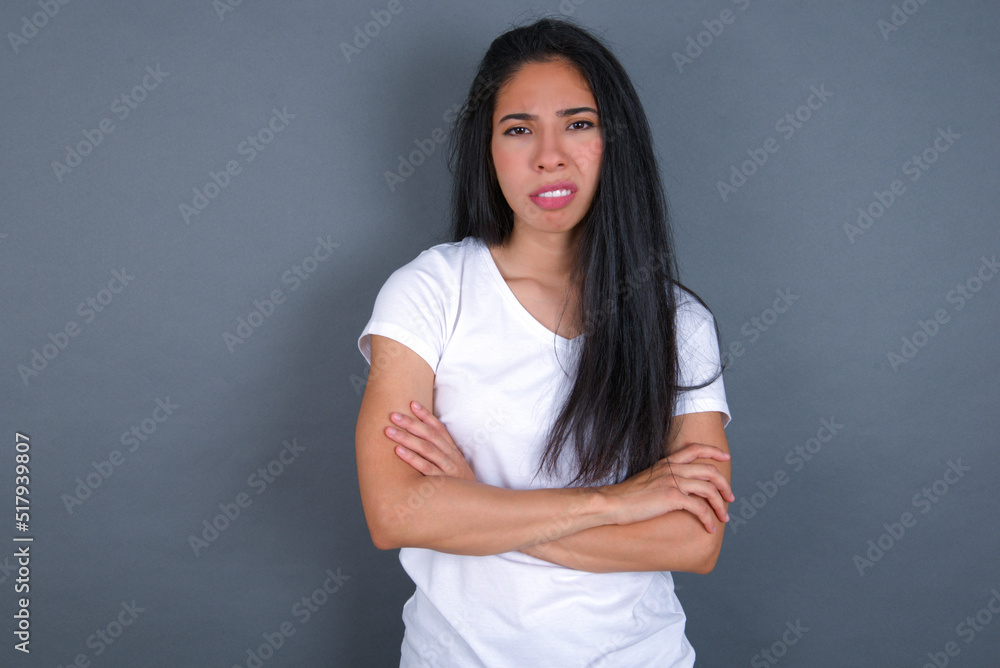 young beautiful brunette woman wearing white t-shirt over grey background frowning his face in displeasure, keeping arms folded, waiting for an explanation. young beautiful brunette woman wearing white t-shirt over grey background frowning his face in displeasure, keeping arms folded, waiting for an explanation.