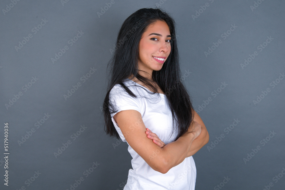 Image of cheerful young beautiful brunette woman wearing white t-shirt over grey background with arms crossed. Looking and smiling at the camera. Confidence concept. Image of cheerful young beautiful brunette woman wearing white t-shirt over grey background with arms crossed. Looking and smiling at the camera. Confidence concept.