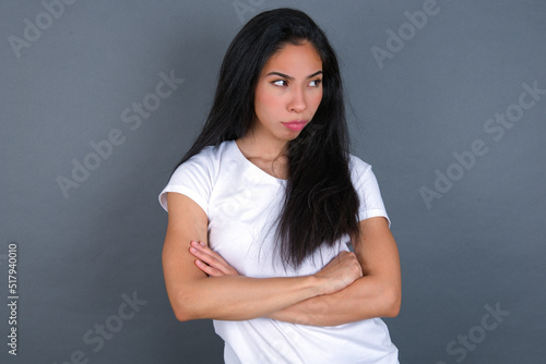 Displeased young beautiful brunette woman wearing white t-shirt over grey background with bad attitude, arms crossed looking sideways. Negative human emotion facial expression feelings.