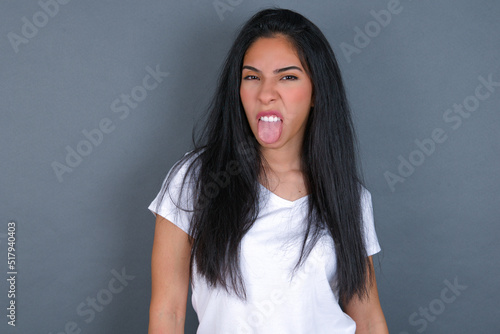 Body language. Disgusted stressed out young beautiful brunette woman wearing white t-shirt over grey background, frowning face, demonstrating aversion to something.