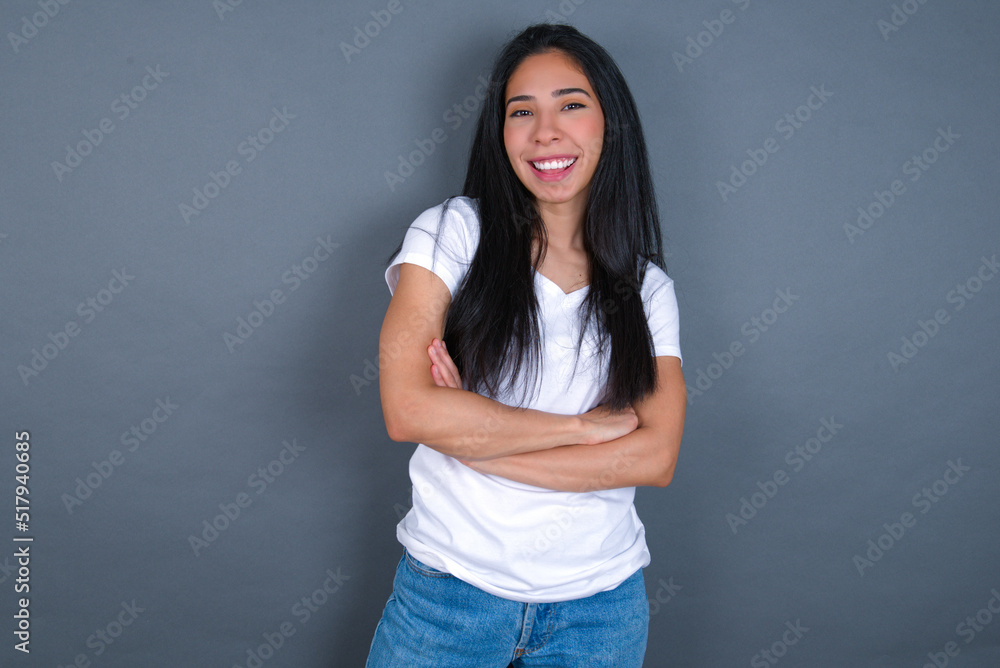 young beautiful brunette woman wearing white t-shirt over grey background being happy smiling and crossed arms looking confident at the camera. Positive and confident person. young beautiful brunette woman wearing white t-shirt over grey background being happy smiling and crossed arms looking confident at the camera. Positive and confident person.