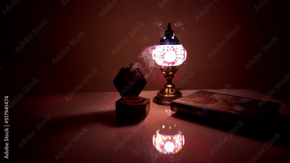 Arabian lamp next to a vessel containing incense lit with smoke and a closed book on a table with dim warm light Arabian lamp next to a vessel containing incense lit with smoke and a closed book on a table with dim warm light