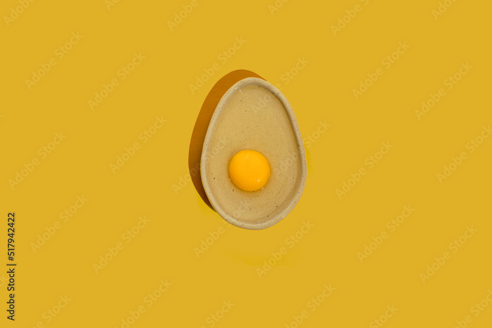 Avocado shaped ceramic plate with raw egg yolk on a bright yellow color background with copy space. Healthy dieting idea.