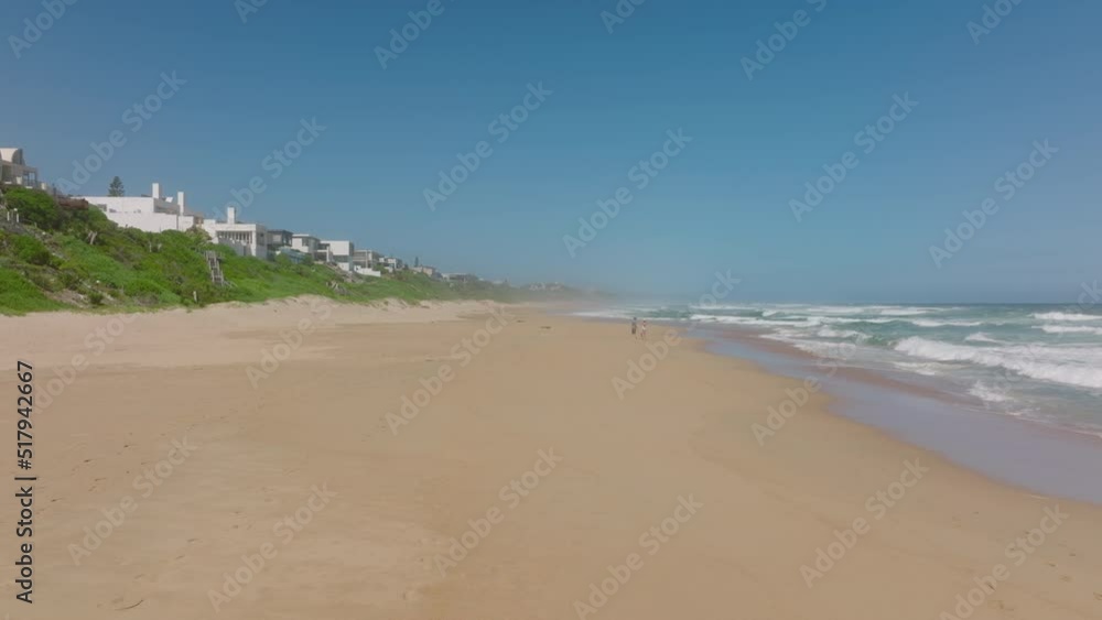 Couple strolling on beach along rolling waves. Forwards fly along coast, houses near sea. South Africa Couple strolling on beach along rolling waves. Forwards fly along coast, houses near sea. South Africa
